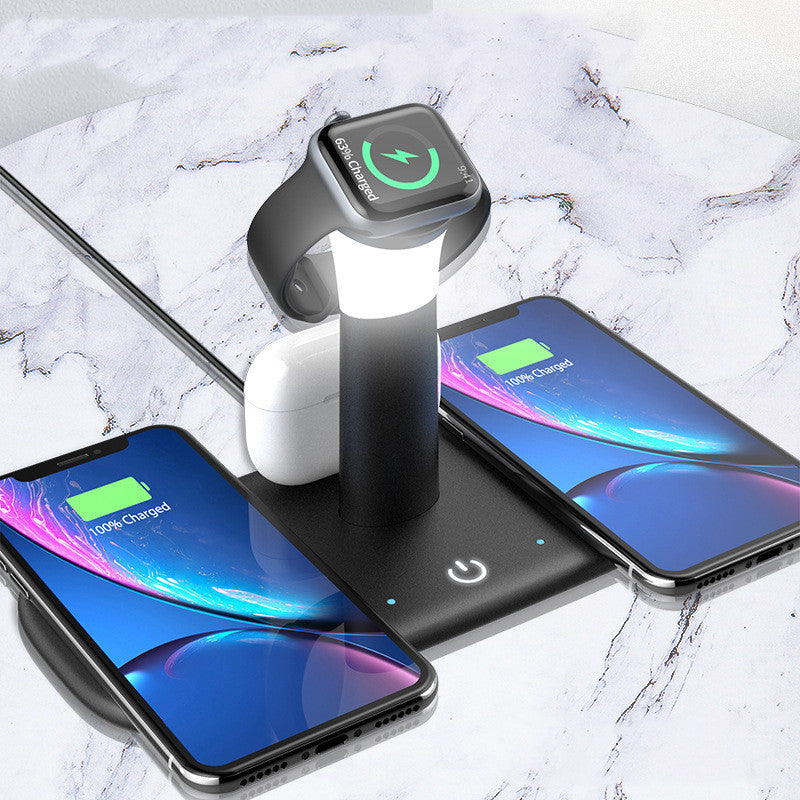 Black 4-in-1 wireless charging station with a central lamp, powering two smartphones, an Apple Watch, and white earbuds.