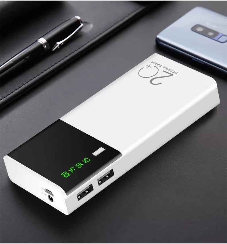 White and black rectangular power bank (20+) featuring a green digital display and dual USB output ports on a dark desk.