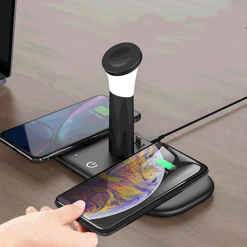 Black wireless charging pad with an integrated white lamp, charging two smartphones on a wooden table.
