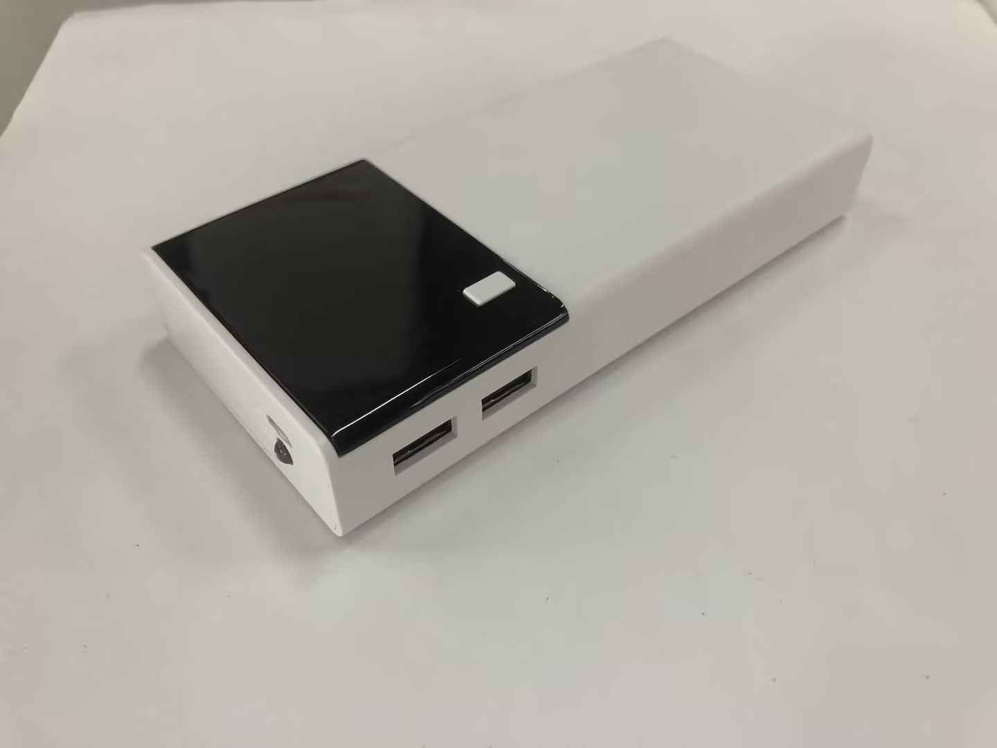 White rectangular power bank featuring a glossy black panel, two USB output ports, and a small white button.