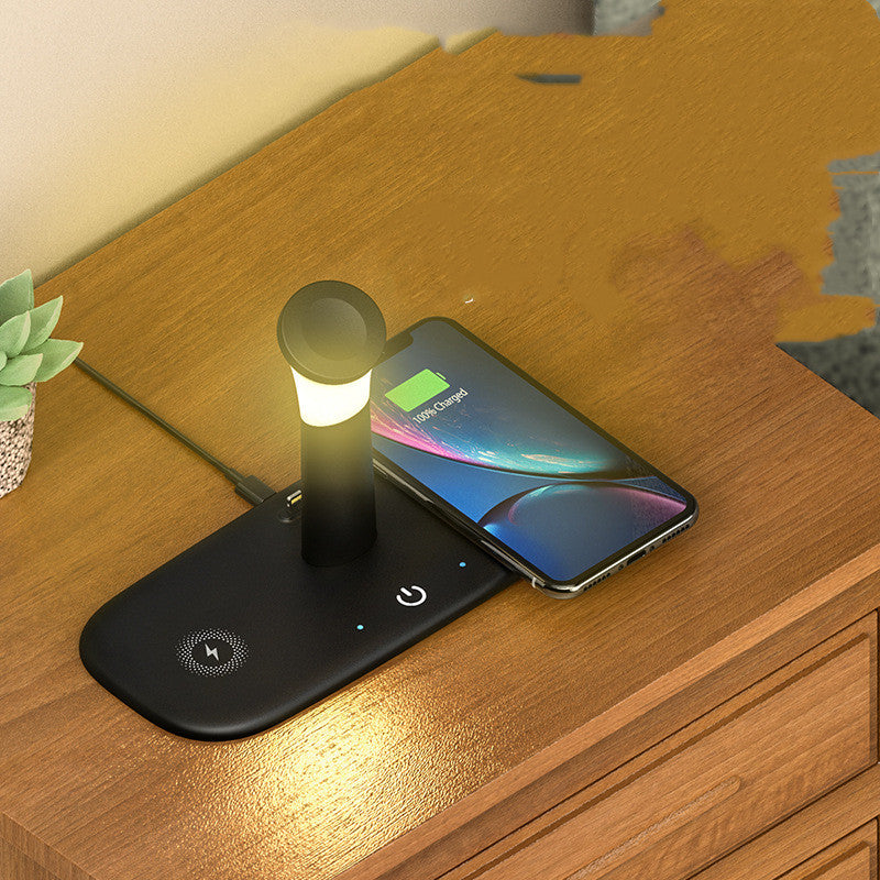Black wireless charging pad and cylindrical lamp on a wood nightstand, charging a smartphone displaying "100% Charged."