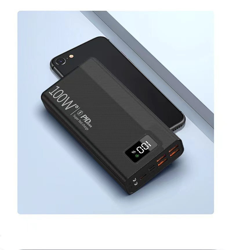 Black, 100W super fast charge power bank with an LED display showing 100%, resting diagonally over a black smartphone.